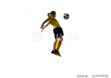 Dynamic image of girl in yellow jersey and black shorts playing soccer game, kicking ball mid-air with chest against white studio background Dynamic image of girl in yellow jersey and black shorts playing soccer game, kicking ball mid-air with chest against white studio background 123549356
