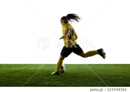 Young sportive girl, child in yellow jersey and black shorts in motion on grassy surface, dribbling ball against white studio background Young sportive girl, child in yellow jersey and black shorts in motion on grassy surface, dribbling ball against white studio background 123549382