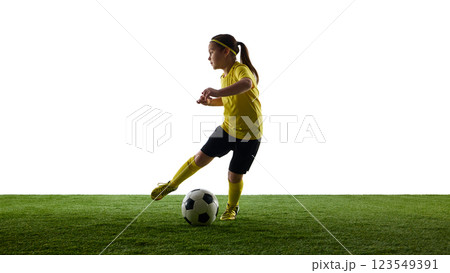 Dynamic image of child, girl in yellow jersey and black shirts in motion on grassy surface, dribbling ball against white studio background 123549391