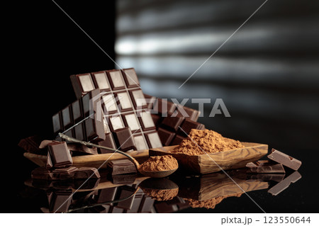 Broken bitter chocolate bars and wooden dish with cocoa powder. Broken bitter chocolate bars and wooden dish with cocoa powder. 123550644