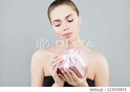 Pretty young happy woman holding gift present box on grey studio wall background Pretty young happy woman holding gift present box on grey studio wall background 123550655