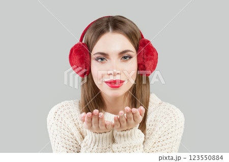 Cute woman wearing red fluffy ear muffs blowing kiss, fashion beauty portrait 123550884