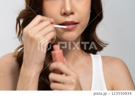 Beauty routine of an Asian woman applying lip gloss for a flawless look during a skincare session 123550934