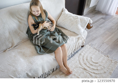 Happy little girl with cat sitting on sofa indoor Happy little girl with cat sitting on sofa indoor 123550970