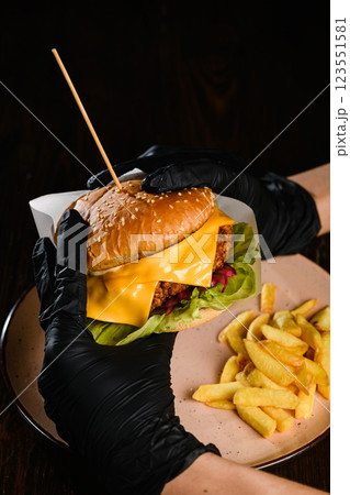 Hands in black gloves holding burger on dark background. 123551581