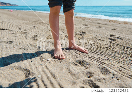 Barefoot Child Standing on a Sunlit Beach with Ocean View 123552421