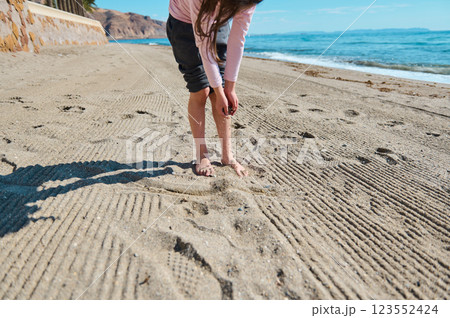 Young Girl Playing Alone on a Beautiful Sunlit Sandy Beach Near the Ocean Young Girl Playing Alone on a Beautiful Sunlit Sandy Beach Near the Ocean 123552424