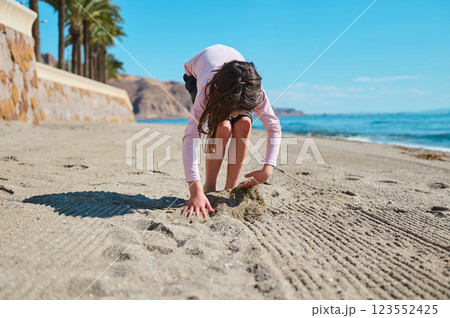 Young Girl Playing with Sand on a Sunny Beach Near the Ocean 123552425
