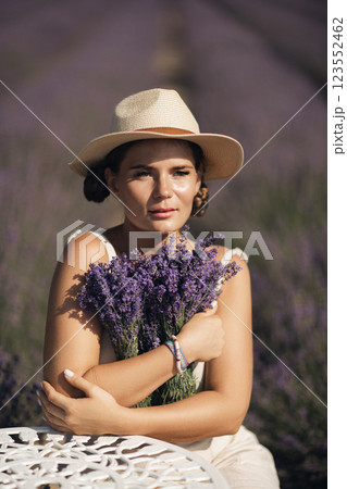 woman sitting in a field of lavender and wearing a straw hat. She is smiling and holding a bouquet of flowers. Scene is peaceful and serene, as the woman is surrounded by the beauty of nature 123552462