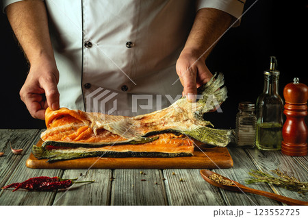 A chef expertly prepares a salmon fillet, showcasing the fish's vibrant colors. Around him are various condiments and tools, highlighting the art of culinary creativity in a cozy kitchen A chef expertly prepares a salmon fillet, showcasing the fish's vibrant colors. Around him are various condiments and tools, highlighting the art of culinary creativity in a cozy kitchen 123552725