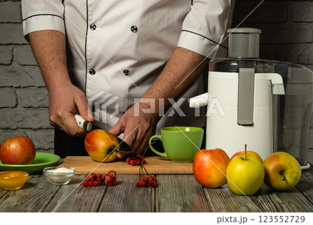 Experienced chef in white uniform cutting red apple for juice in electric juicer. Making tasty and healthy drink from fresh apples in restaurant or hotel kitchen for lunch. Fruit diet Experienced chef in white uniform cutting red apple for juice in electric juicer. Making tasty and healthy drink from fresh apples in restaurant or hotel kitchen for lunch. Fruit diet 123552729