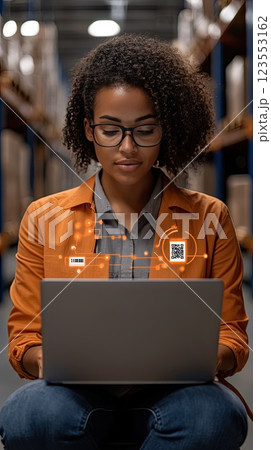 A female worker in a warehouse scans boxes with a barcode scanner while using a laptop to update the inventory system 123553162