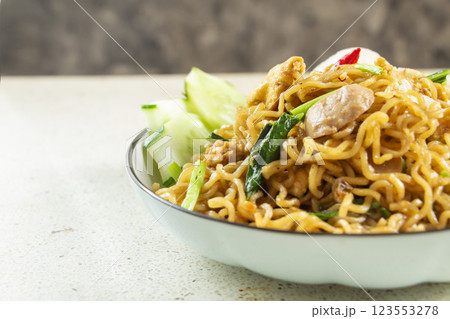 closeup of fried noodles filled with meatballs, fried egg, cucumber and vegetables on white marble table texture, negative space 123553278
