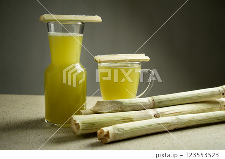 two glasses of sugarcane juice drink on isolated white marble table, pile of peeled sugarcane stalks two glasses of sugarcane juice drink on isolated white marble table, pile of peeled sugarcane stalks 123553523