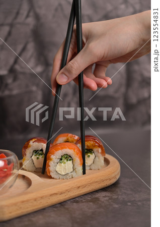 Set of sushi roll with rice and fish on wooden serving board. Woman's hand holding sushi roll used chopsticks. Dark black texture background with copy space. Japan menu. Asian food 123554831