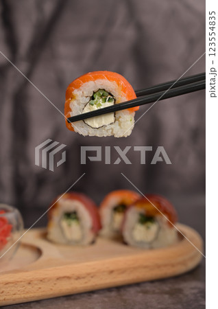 Set of sushi roll with rice and fish on wooden serving board. Chopsticks holding sushi roll. Close up. Dark black texture background with copy Set of sushi roll with rice and fish on wooden serving board. Chopsticks holding sushi roll. Close up. Dark black texture background with copy 123554835