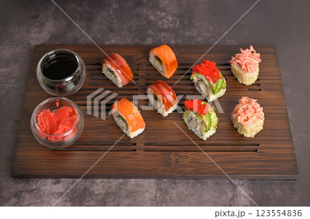 Set of sushi roll with rice and fish, soy sauce and ginger into a glass bowl on wooden serving board. Dark black texture background with copy space. Japan menu. Asian food 123554836