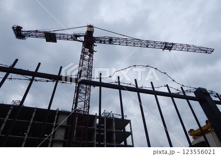 Tower construction crane over an unfinished high-rise building on a construction site behind a barbed wire fence Tower construction crane over an unfinished high-rise building on a construction site behind a barbed wire fence 123556021
