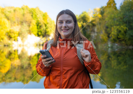 Traveler hiker woman holding smartphone in a hand and using GPS app with trekking in autumn mountains outdoor.  123556119