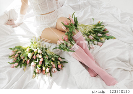 Close-up of a woman's legs in pink socks with fresh tulips, sitting on a white bed in soft natural light, creating a dreamy, romantic spring mood. Close-up of a woman's legs in pink socks with fresh tulips, sitting on a white bed in soft natural light, creating a dreamy, romantic spring mood. 123558130