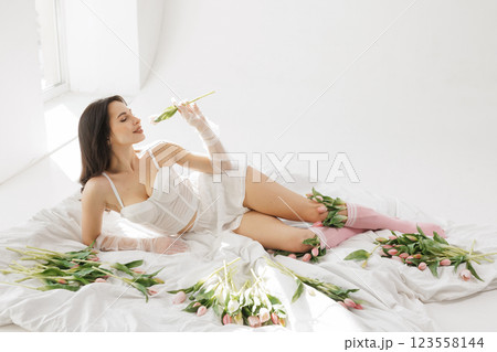 Elegant woman in white lingerie lying on bed with tulips, enjoying flowers in soft natural light, romantic and feminine aesthetic 123558144