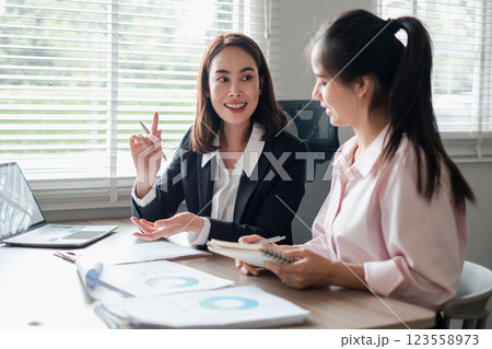 Two businesswomen engaged in a discussion over reports in a bright office environment, showcasing teamwork and collaboration. Two businesswomen engaged in a discussion over reports in a bright office environment, showcasing teamwork and collaboration. 123558973