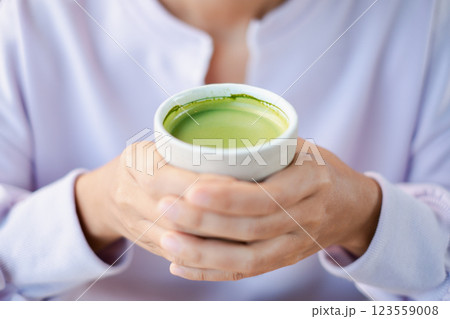 A person holding a cup of vibrant matcha green tea, showcasing warmth and relaxation in a serene environment. 123559008