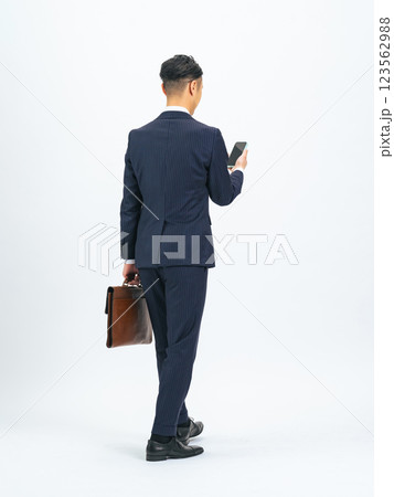 スマホを見ながら歩くミドル男性ビジネスパーソンの後ろ姿の全身写真 スマホを見ながら歩くミドル男性ビジネスパーソンの後ろ姿の全身写真 123562988
