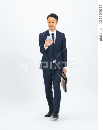 スマホを見ながら歩くミドル男性ビジネスパーソンの全身写真 123563033