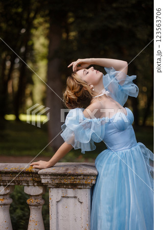 Romantic Woman in a Light Blue Gown Posing on a stone balustrade in a picturesque garden. 123563706