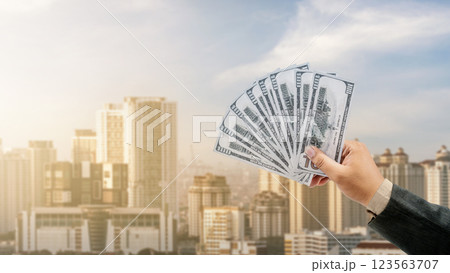 Businessman holding dollar bills with a modern city background. Concept of business, finance, and economy 123563707