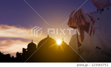 Muslim man praying with prayer beads with a view of the silhouette of the mosque with sunlight in the sunset scene background. Concept of Religion, Spiritual or Ramadan Muslim man praying with prayer beads with a view of the silhouette of the mosque with sunlight in the sunset scene background. Concept of Religion, Spiritual or Ramadan 123563751