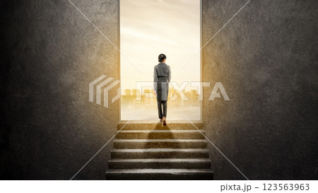 Rear view of an Asian Indonesian businesswoman walking on stairs while looking at the cityscape skyline from the gap of the wall. Concept of business ambition or vision 123563963
