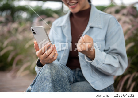 A woman is looking excited while watching video or live streaming on the phone holding in right hand 123564232