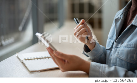 A close up of the left hand holding smartphone with right hand making a fist and holding a pen. 123564268