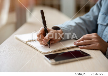 A close up of person noting down or writing down in the notebook with smartphone placing on the table 123564272