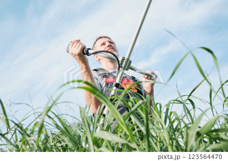 Man in overalls with weed trimmer mowing tall grass on sky background Man in overalls with weed trimmer mowing tall grass on sky background 123564470