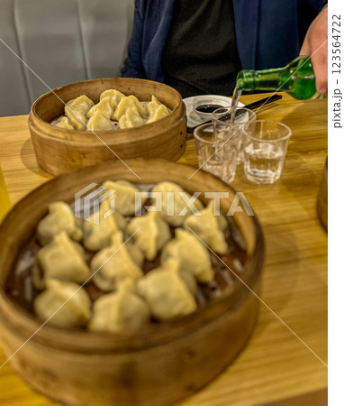 Steamed dumplings in in wooden bamboo steamer like a plate with a glass of juice and bottle of soju at the restaurant 123564722