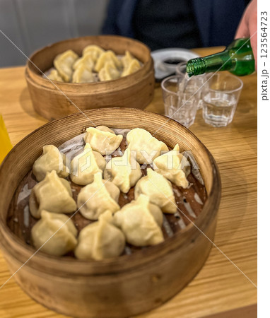 Steamed dumplings in in wooden bamboo steamer like a plate with a glass of juice and bottle of soju at the restaurant Steamed dumplings in in wooden bamboo steamer like a plate with a glass of juice and bottle of soju at the restaurant 123564723