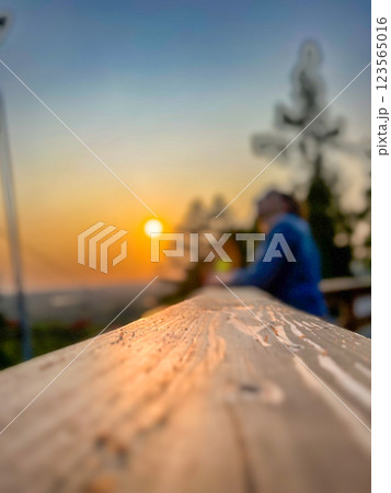 Blur image of woman sitting on wooden terrace with sunset background. 123565016