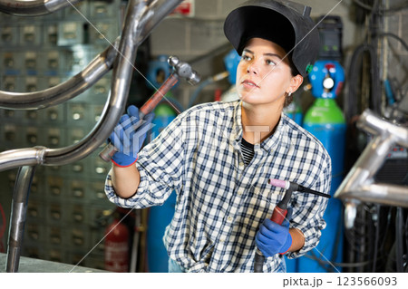 Portrait of a female welder standing with a welding machine and a safety helmet in metal machining workshop Portrait of a female welder standing with a welding machine and a safety helmet in metal machining workshop 123566093