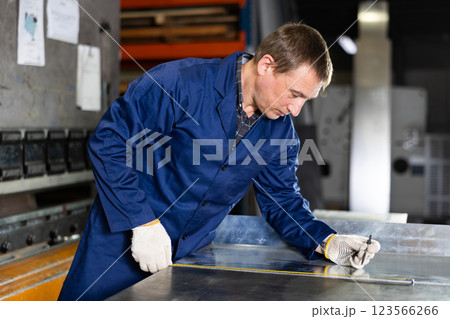 Man measuring sheet of metal with tape measure Man measuring sheet of metal with tape measure 123566266
