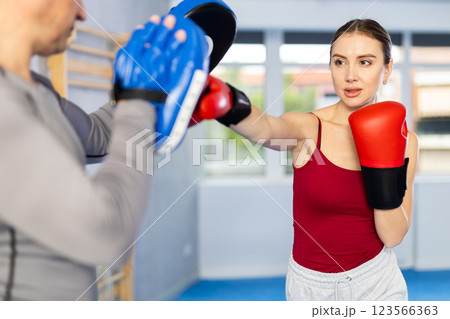 Athletic woman learns to box - hitting punch mitts. Woman with her trainer at gym 123566363