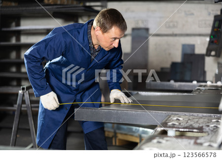 Male worker at metallurgical plant measures an iron sheet using tape measure and marks cutting line Male worker at metallurgical plant measures an iron sheet using tape measure and marks cutting line 123566578
