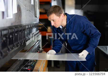 Craftsman positioning metal workpiece on bending machine in workshop Craftsman positioning metal workpiece on bending machine in workshop 123566704