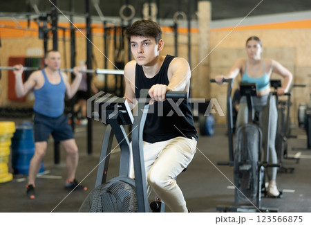Young dedicated man training on exercise bike near other people in gym Young dedicated man training on exercise bike near other people in gym 123566875