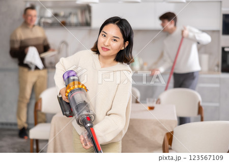Girl vacuuming floor while his relatives help tidy up room 123567109