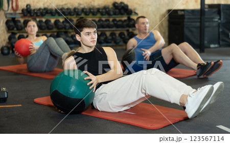 Concentrated guy doing ab exercises with medicine ball in gym Concentrated guy doing ab exercises with medicine ball in gym 123567114