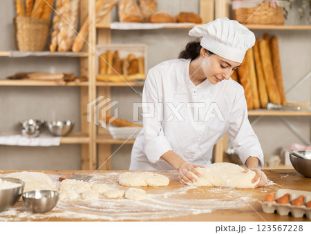 Young woman works as baker, mold baguette from dough, creates long loafs from dough. Young woman works as baker, mold baguette from dough, creates long loafs from dough. 123567228
