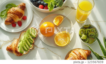 Top-down view of a delicious breakfast spread: avocado toast, fresh orange juice, croissants, and a bowl of berries 123567839